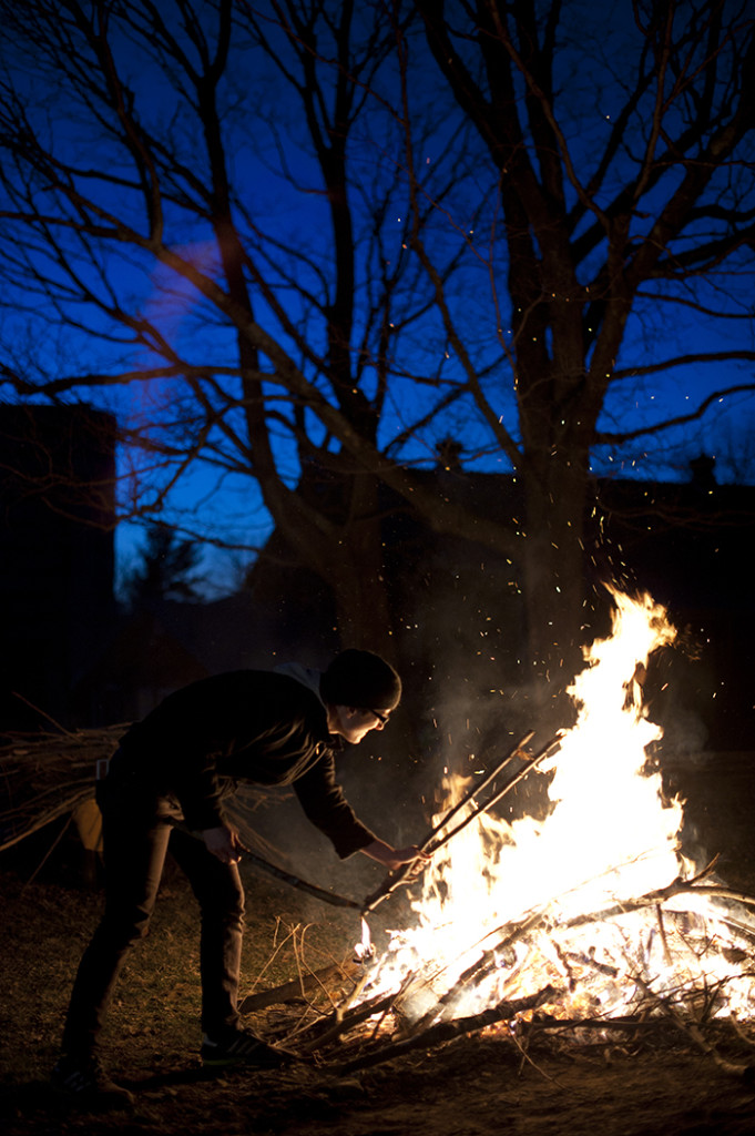 Jay Mounteer stoking an outdoor wood fire against a night sky and bare tree